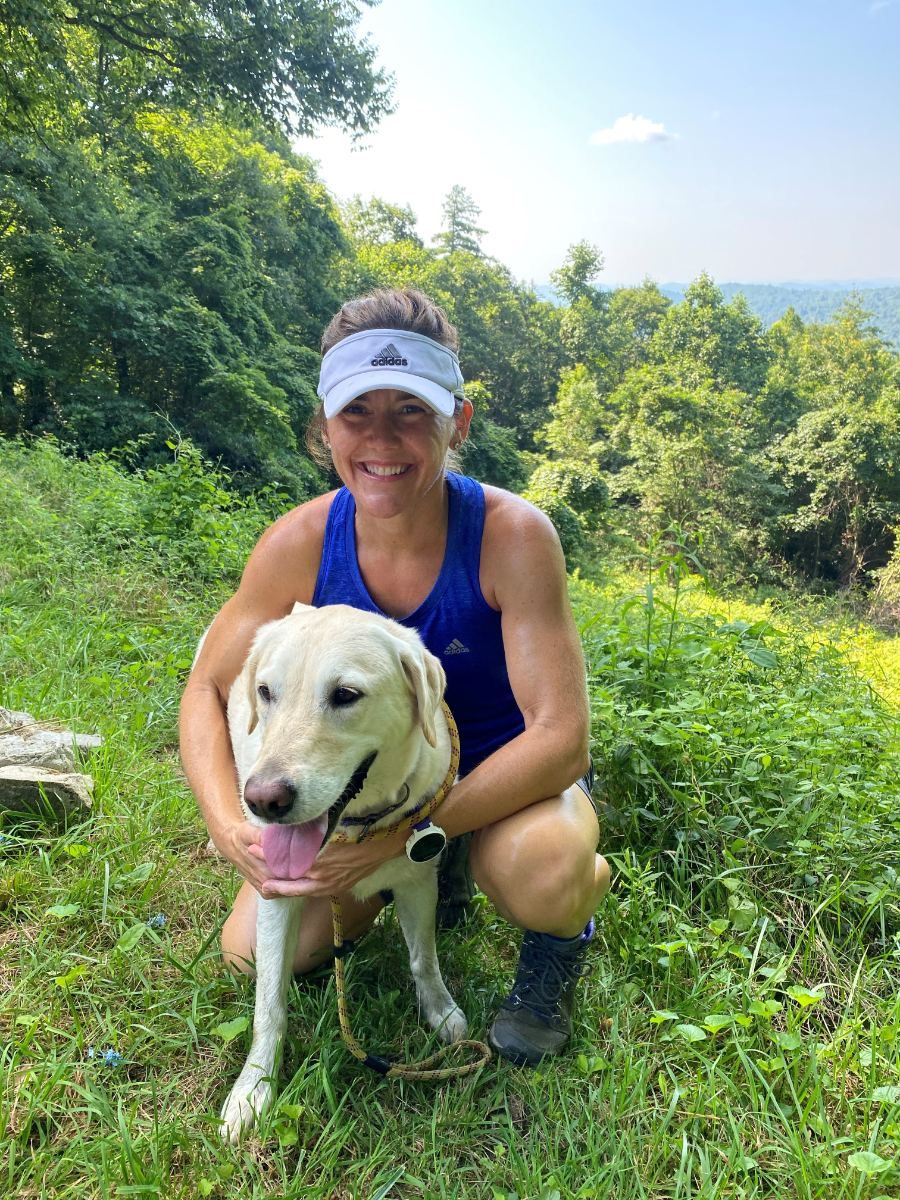 Tracey kneeling on a mountain trail with her yellow lab